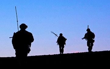 Silhouette of three soliders in the field at dusk against a fading blue sky